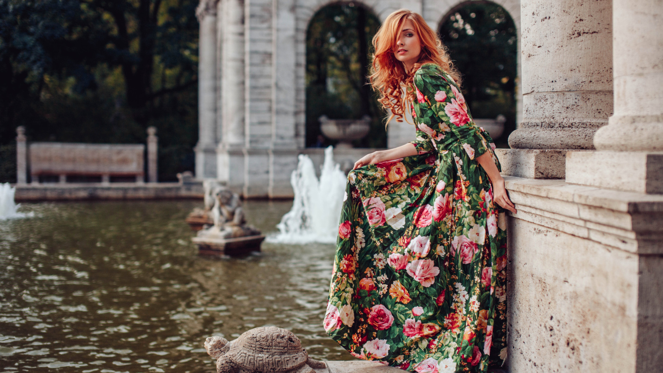 Девушка в красивом цветастом платье у пруда в парке 