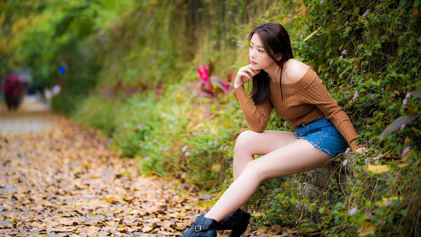 Задумчивая азиатка сидит в парке осенью 