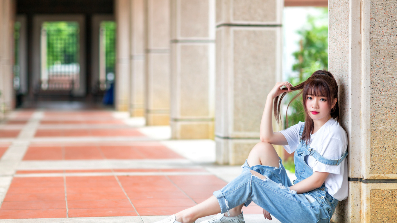 Грустная девушка азиатка сидит у колонны