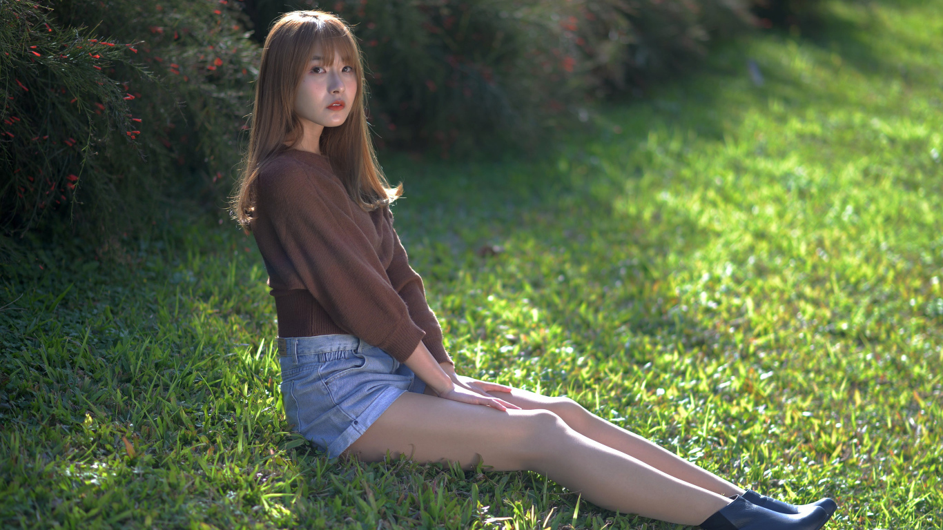 Грустная девушка азиатка сидит на зеленой траве 