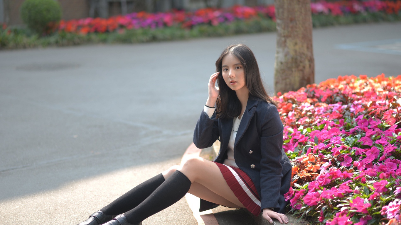 Девушка школьница сидит на земле у клумбы 