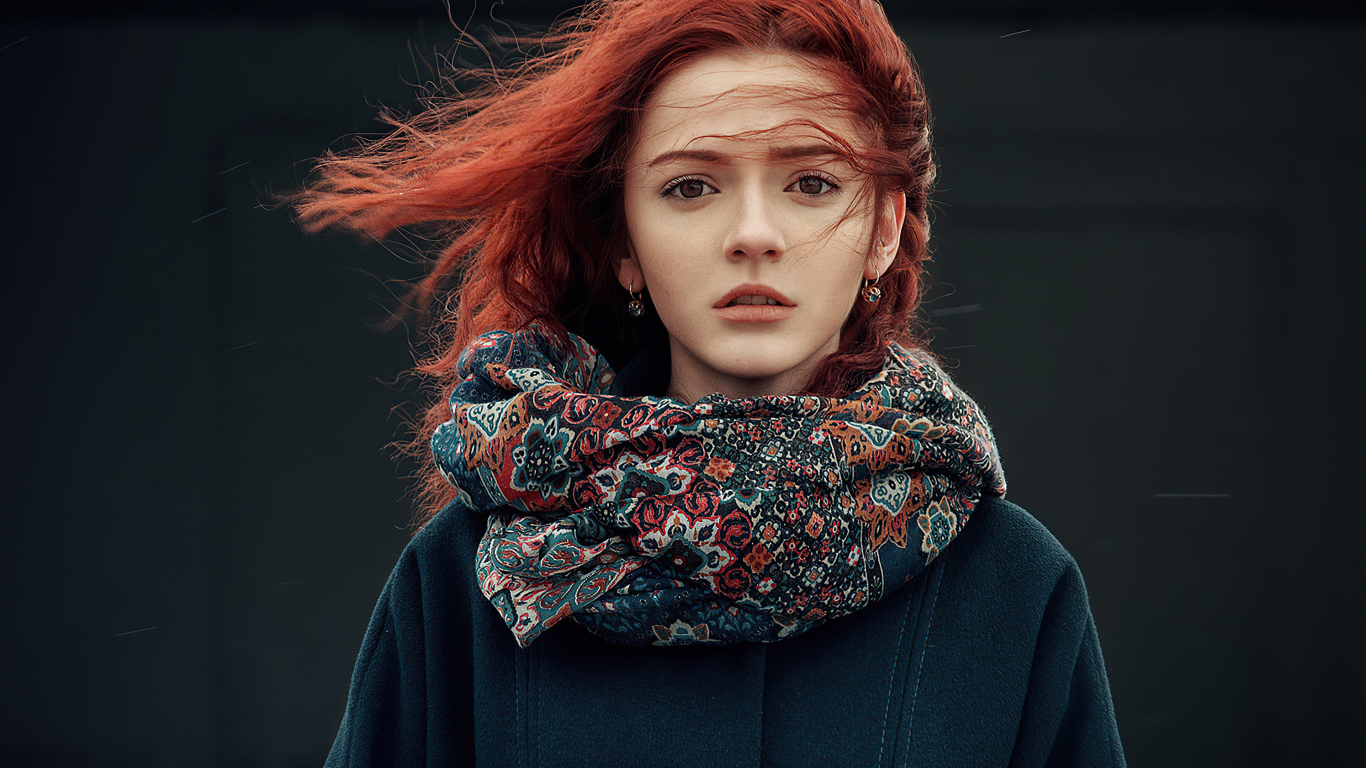 Ветер развивает волосы рыжеволосой девушки в пальто