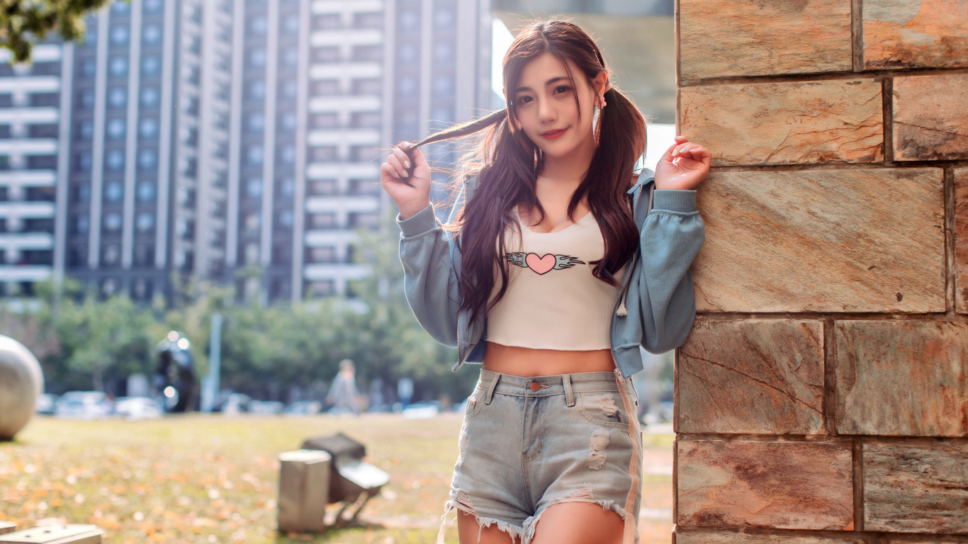 Молодая азиатка в коротких шортах стоит у стены