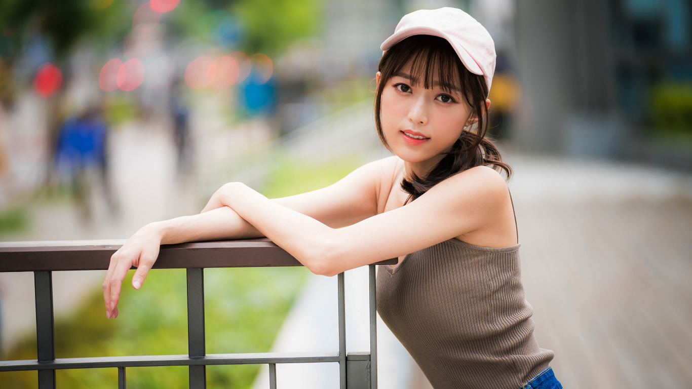 Молодая азиатка в кепке у перил 