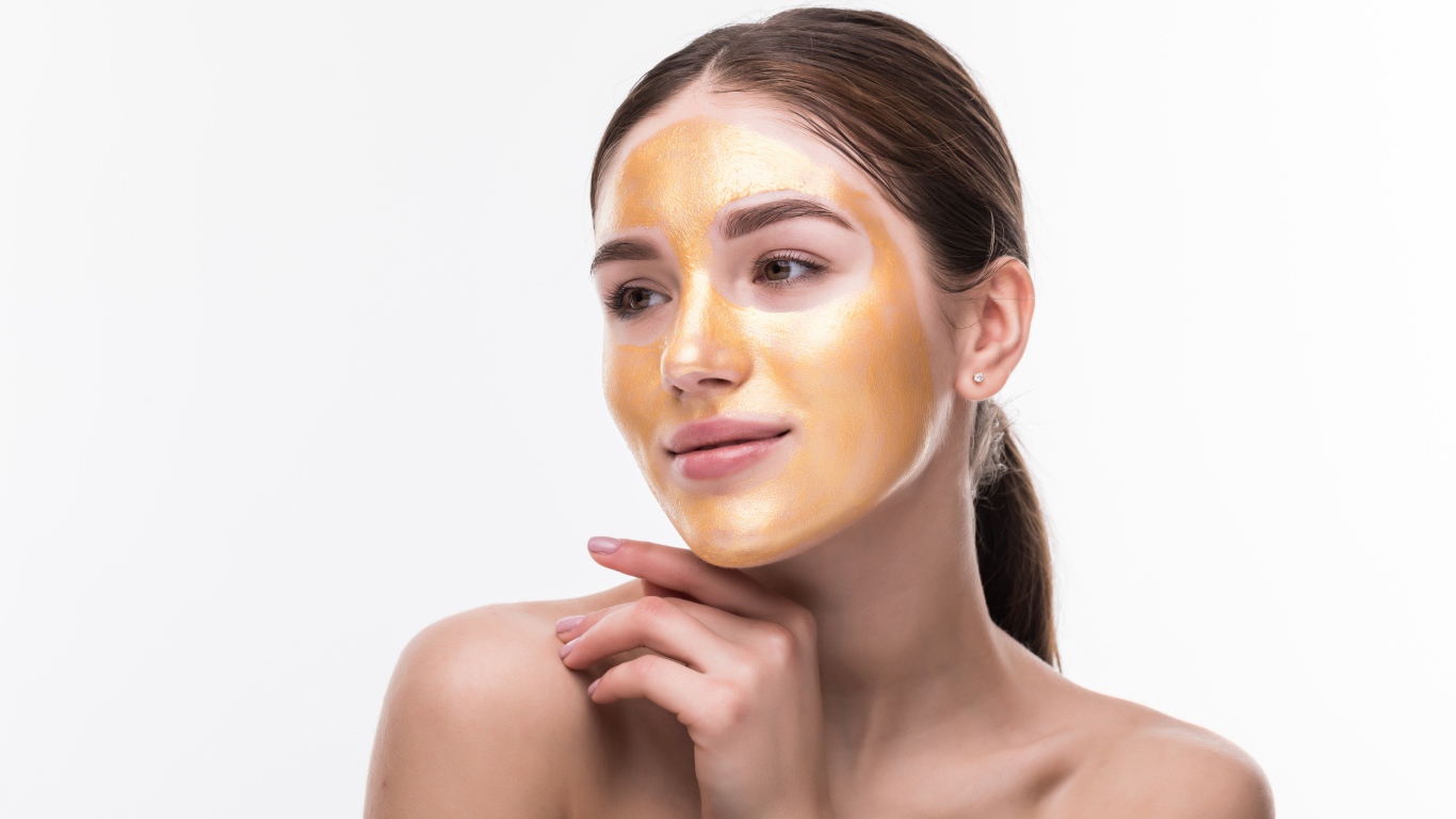 Молодая девушка без макияжа с золотой маской на лице