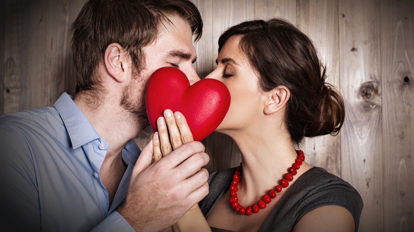 Kiss of a couple in love behind a red heart