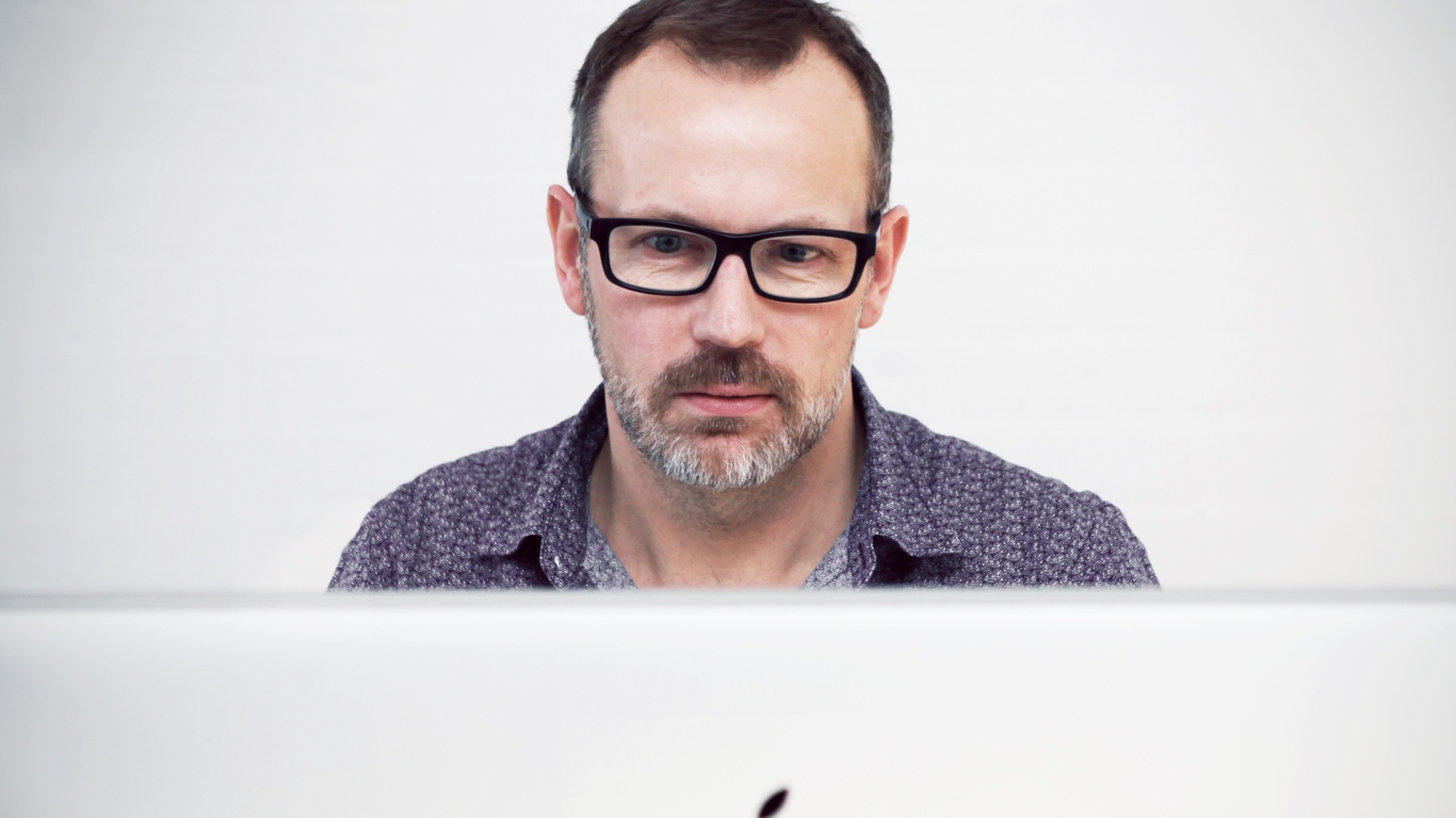 Серьезный мужчина в очках сидит за макбуком