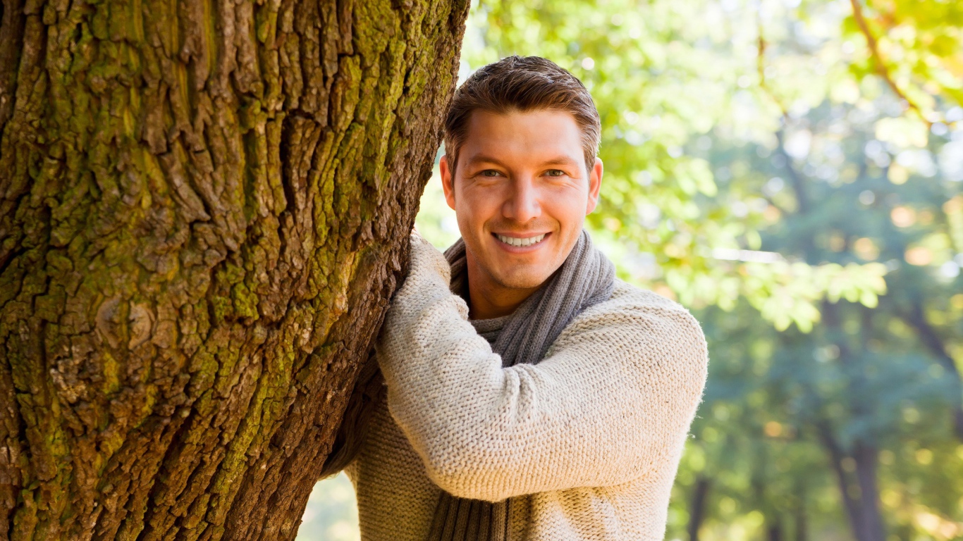 Улыбающийся мужчина стоит у дерева 