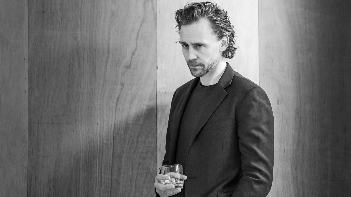 Актер Том Хиддлстон с бокалом в руке на фоне стены