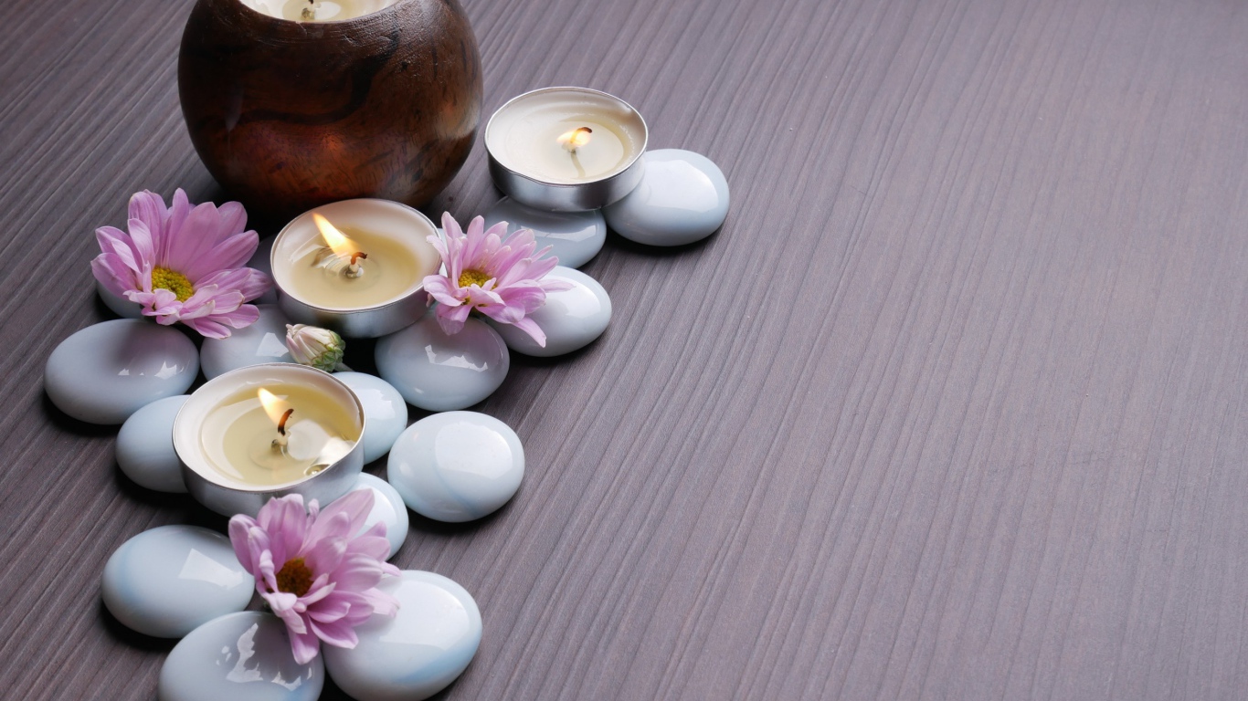 Камни с хризантемами и зажженными свечами на столе 