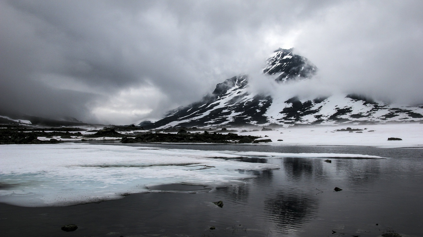 Cold gray fog over a snow-capped mountain by the lake