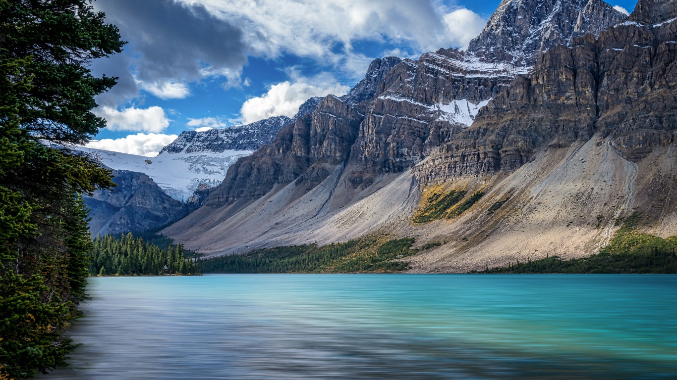 Высокие каменные горы в снегу под голубым небом у озера 