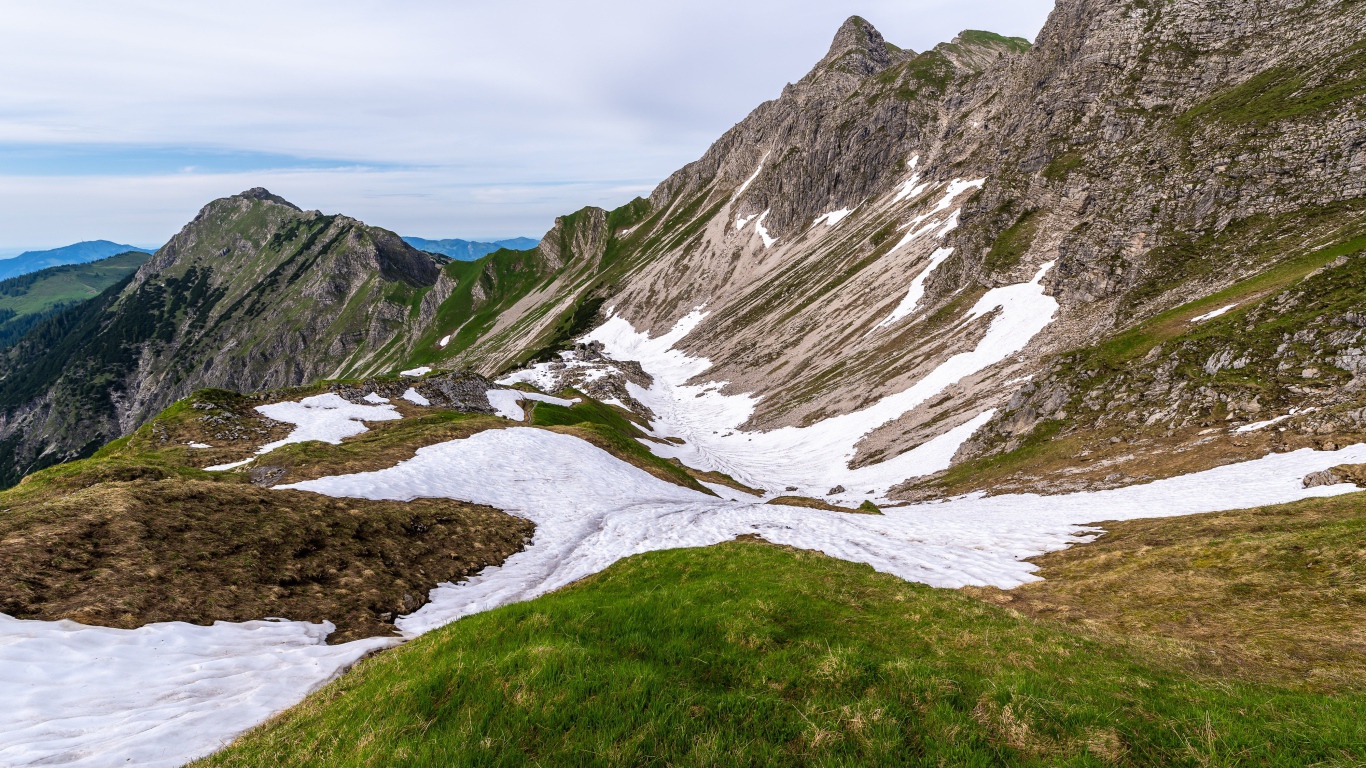 Снег на склонах горы с зеленой травой 