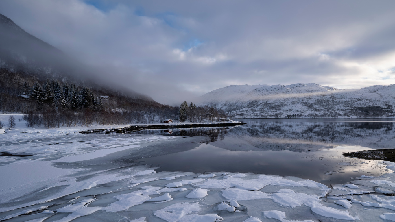 Покрытое льдом холодное озеро у гор в тумане