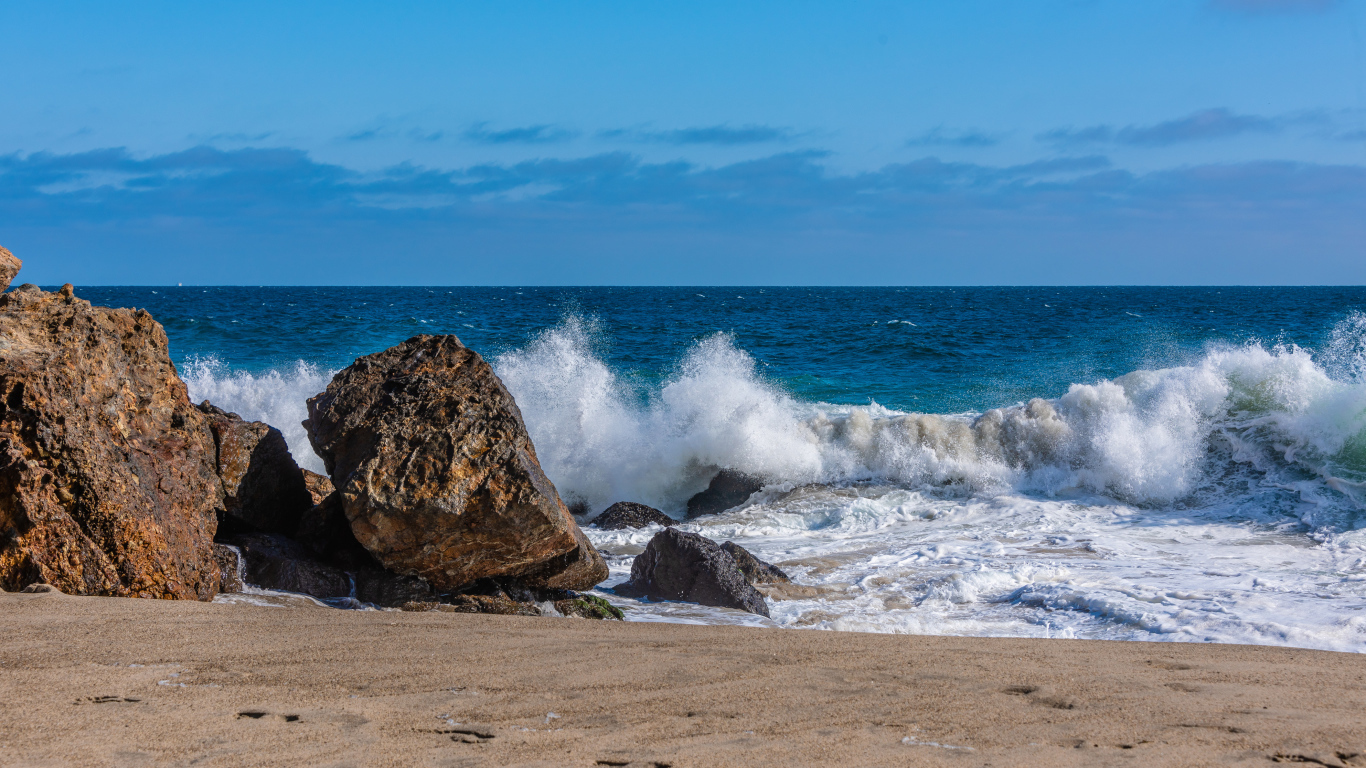Белые морские волны бьются о большие камни на берегу