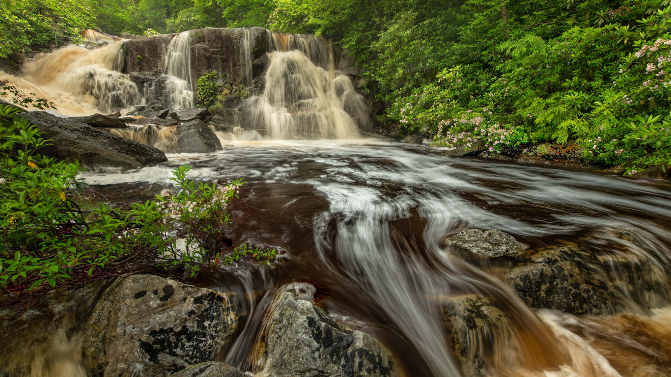 Быстрая холодная вода водопада стекает по большим камням