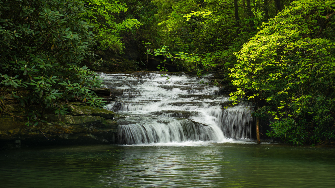 Водопад стекает по каменному каскаду в реку 
