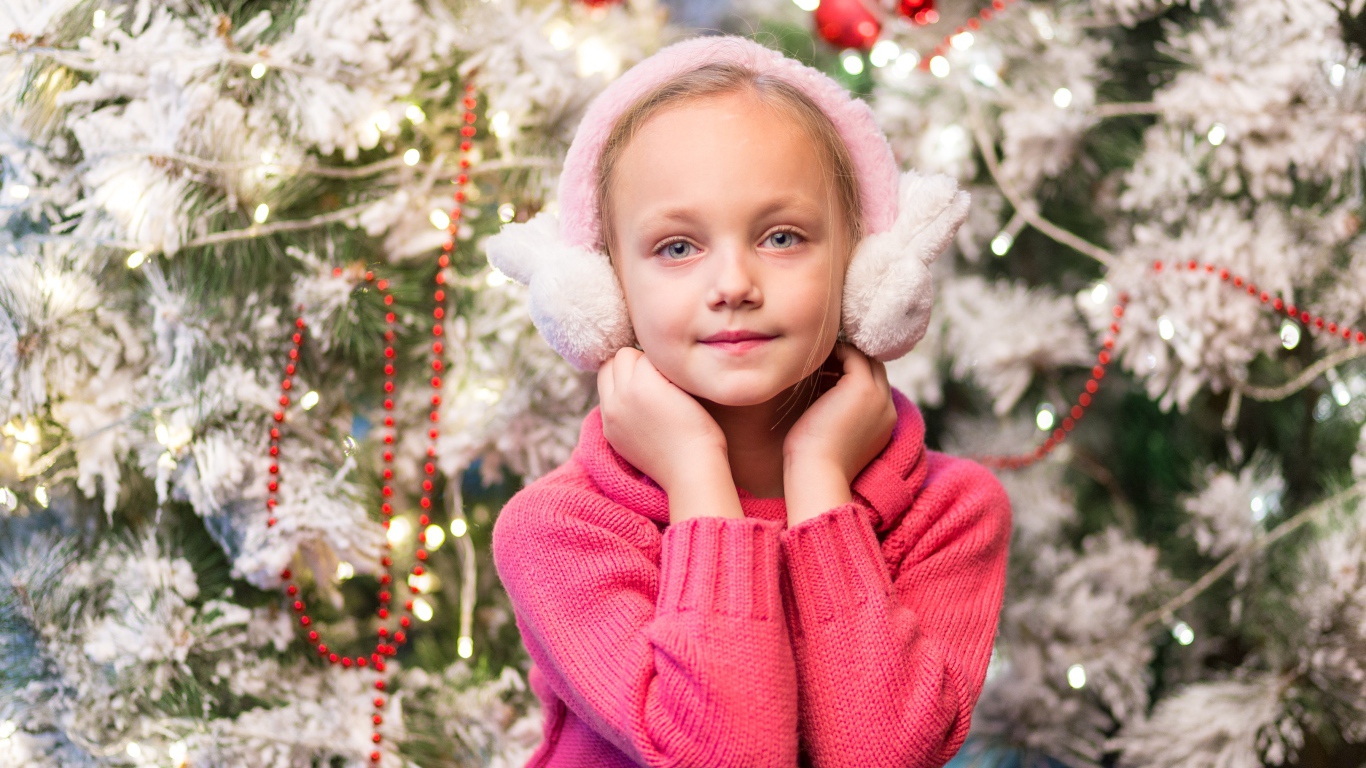 Девочка в розовых наушниках сидит у ели