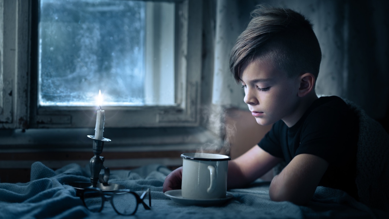 A little boy sitting at a table by the light of a candle