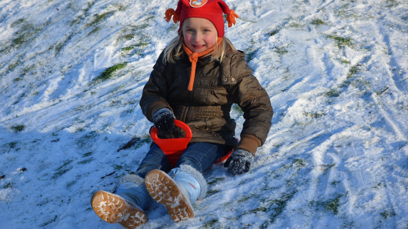 Маленькая девочка катится с горки по снегу