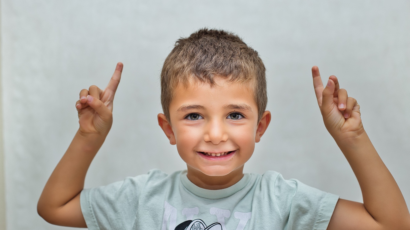 Маленький мальчик поднял руки вверх на сером фоне