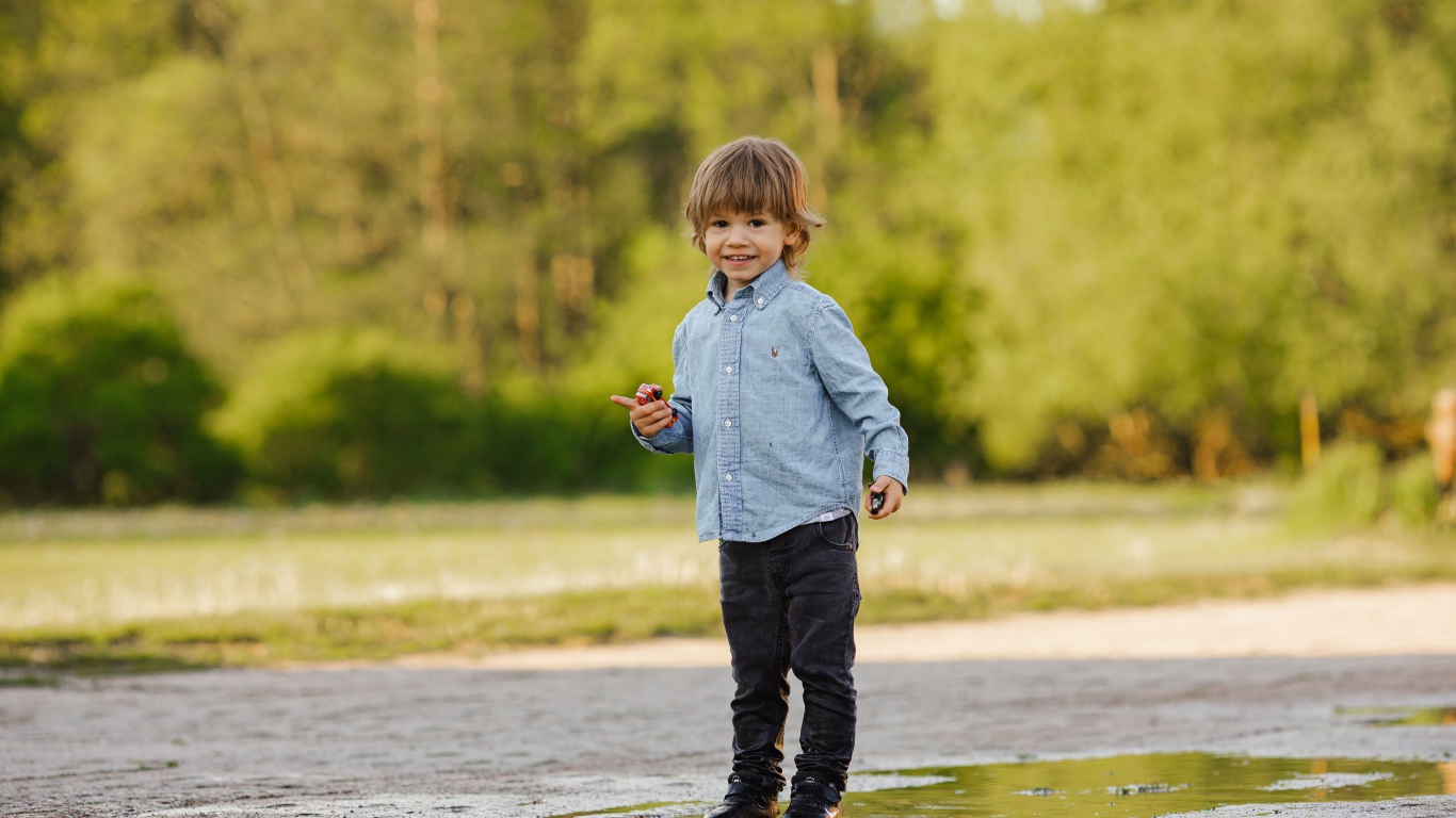 Маленький мальчик стоит в луже на дороге 