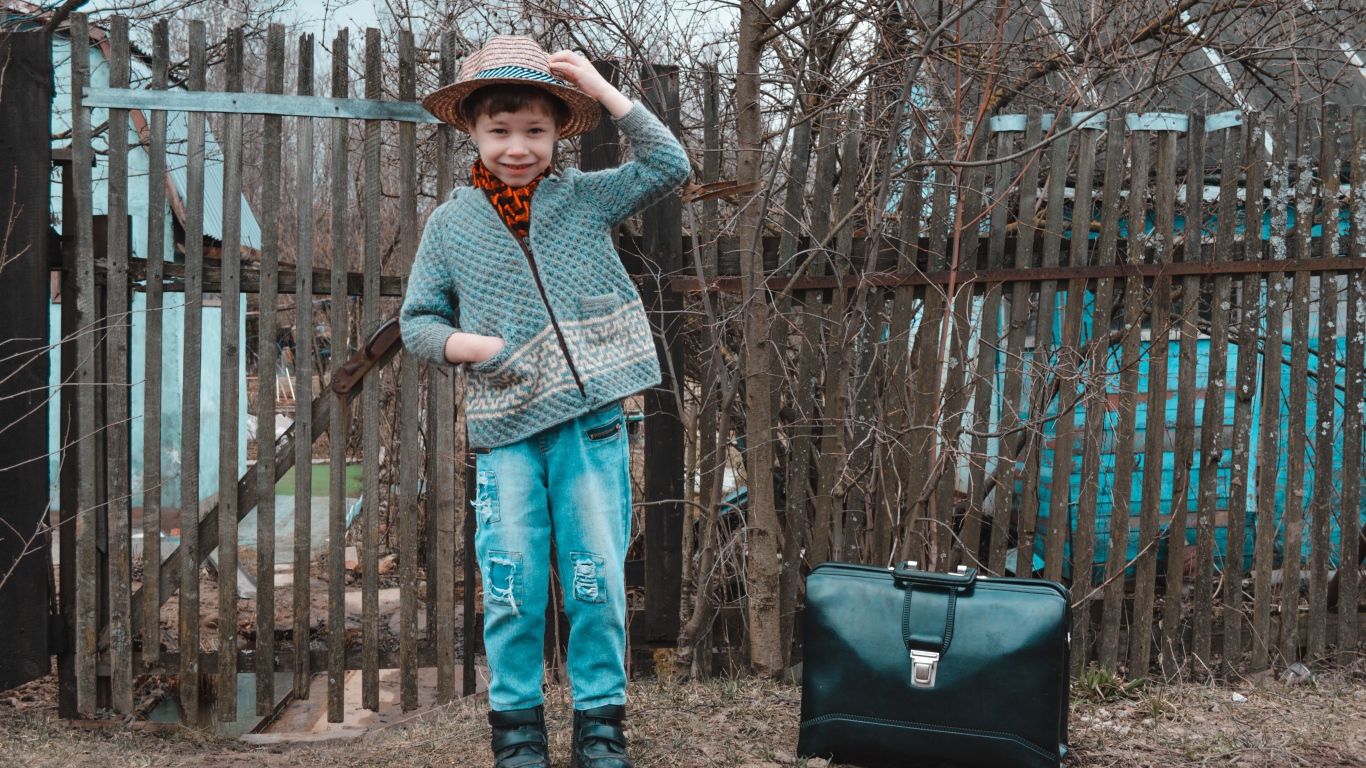 Маленький мальчик с чемоданом у забора