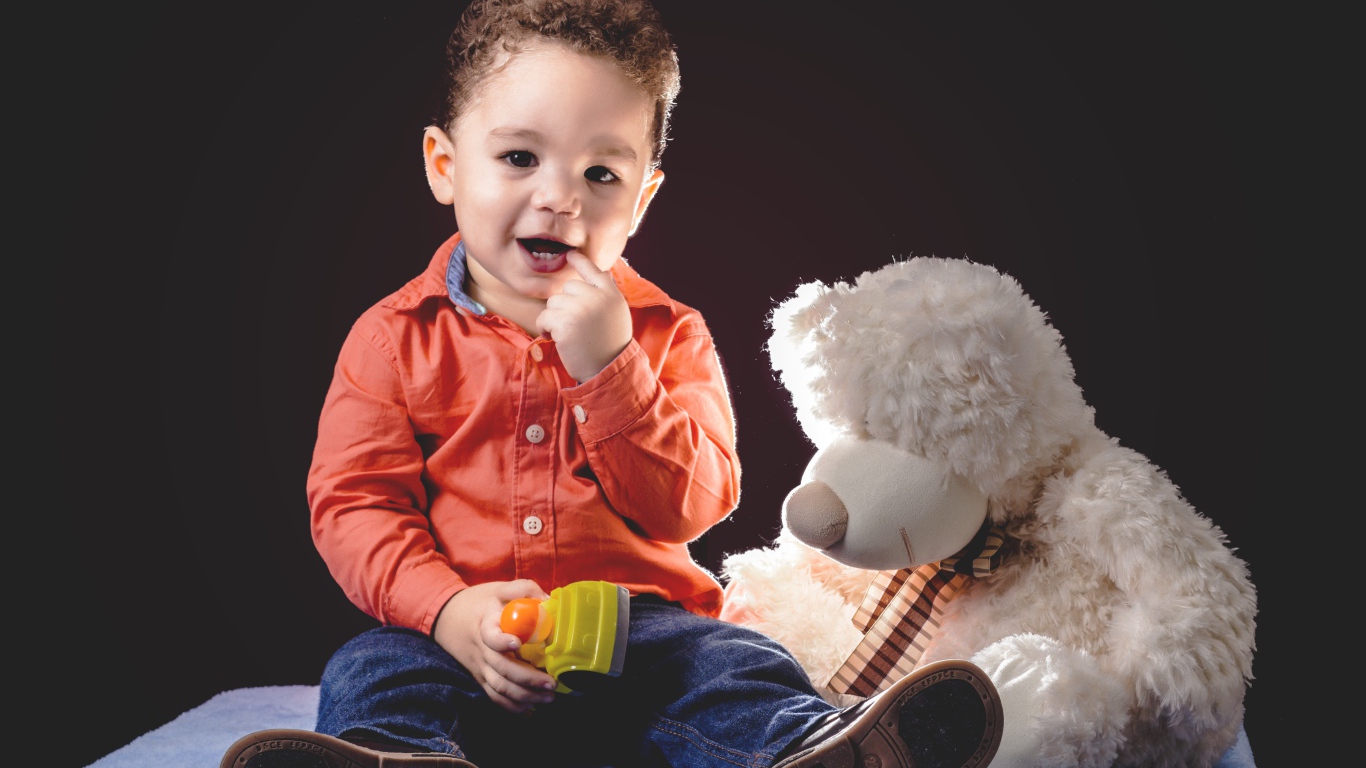 Маленький мальчик с игрушечным медведем на черном фоне