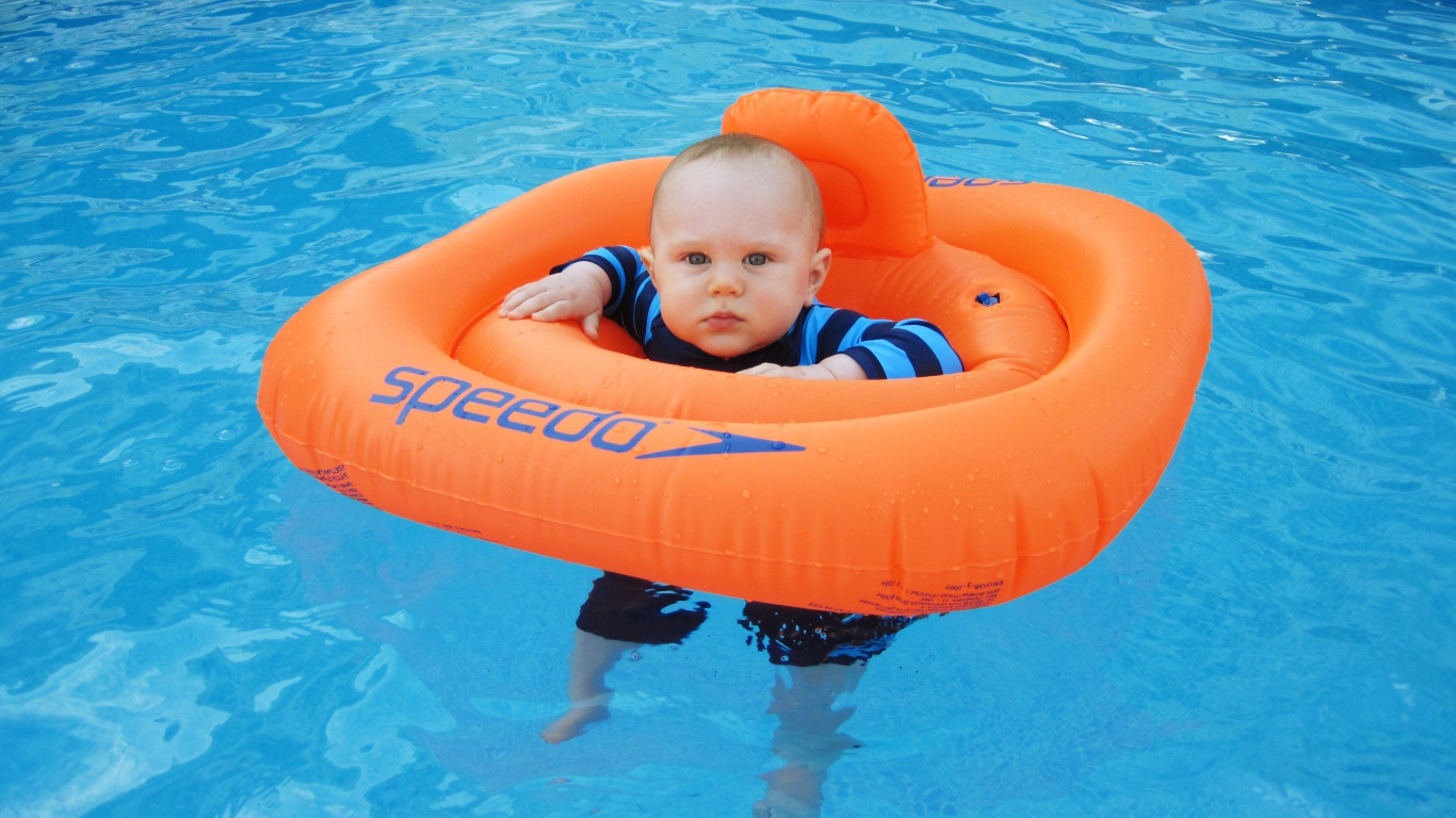 Маленький ребенок с оранжевым спасательным кругом в бассейне