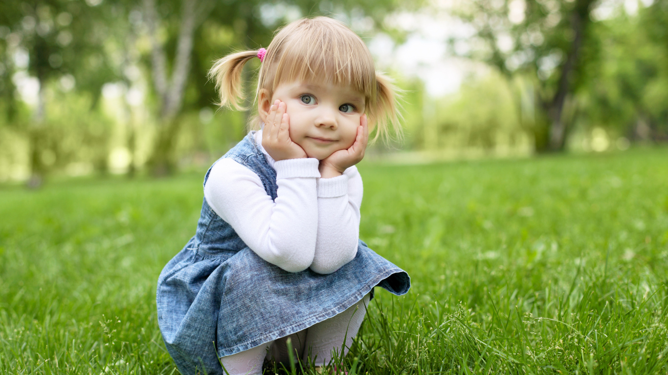 Маленькая девочка в сарафане сидит на траве 