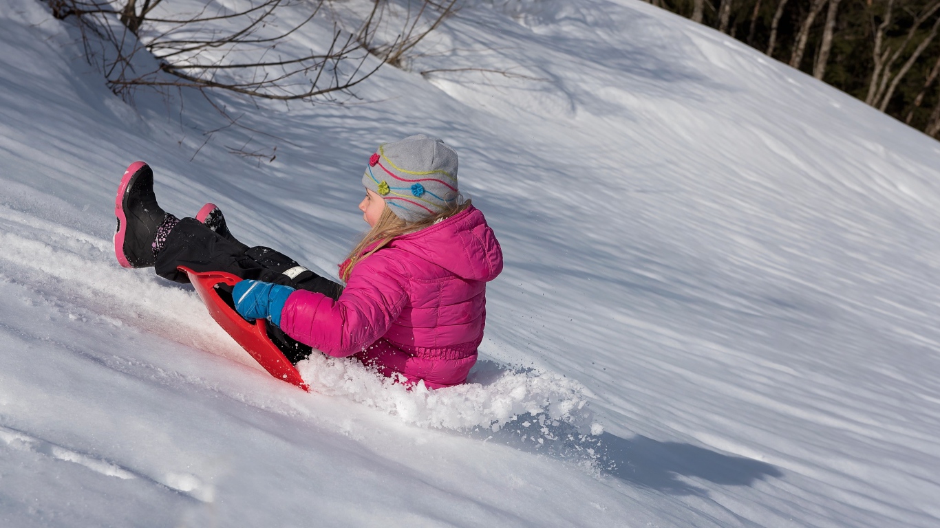 Маленькая девочка катится с заснеженной горки 