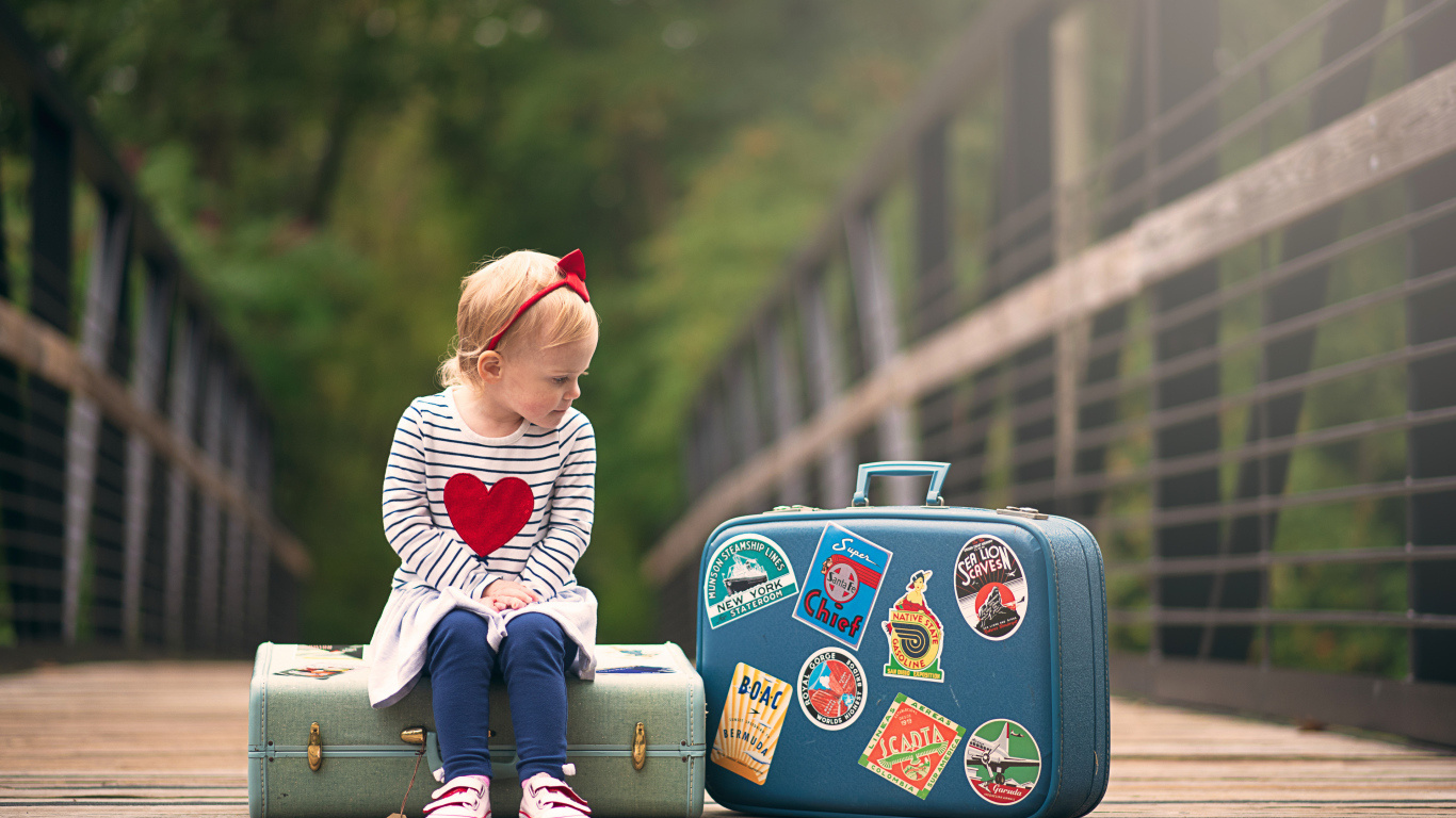 Маленькая девочка сидит на мосту с чемоданами