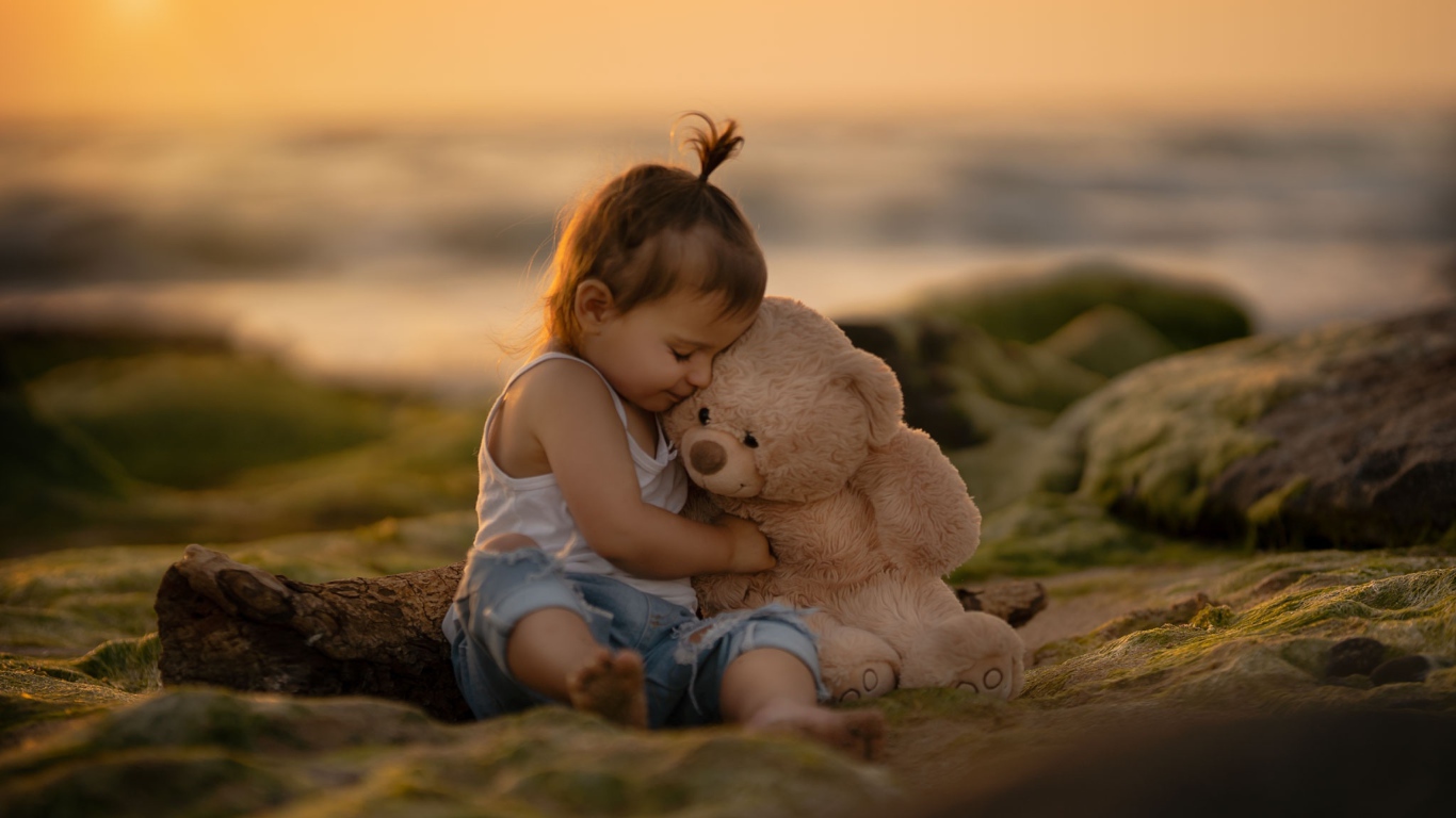 Маленькая девочка с игрушечным медведем сидит на камне