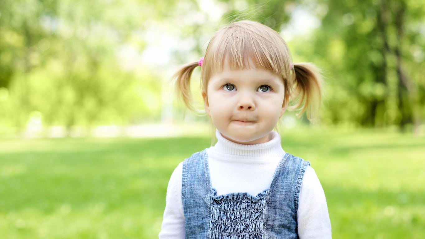 Маленькая девочка с хвостиками на голове в парке 