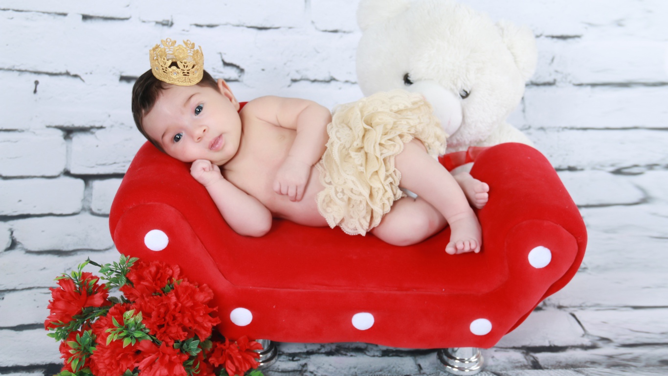 Маленькая принцесса лежит на красном диване у стены 