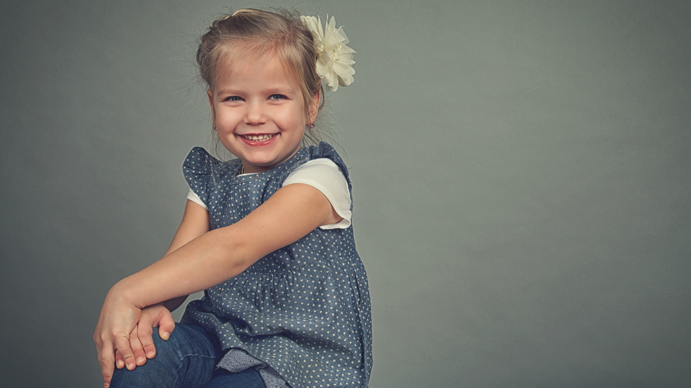 Маленькая улыбающаяся девочка с бантом на сером фоне 
