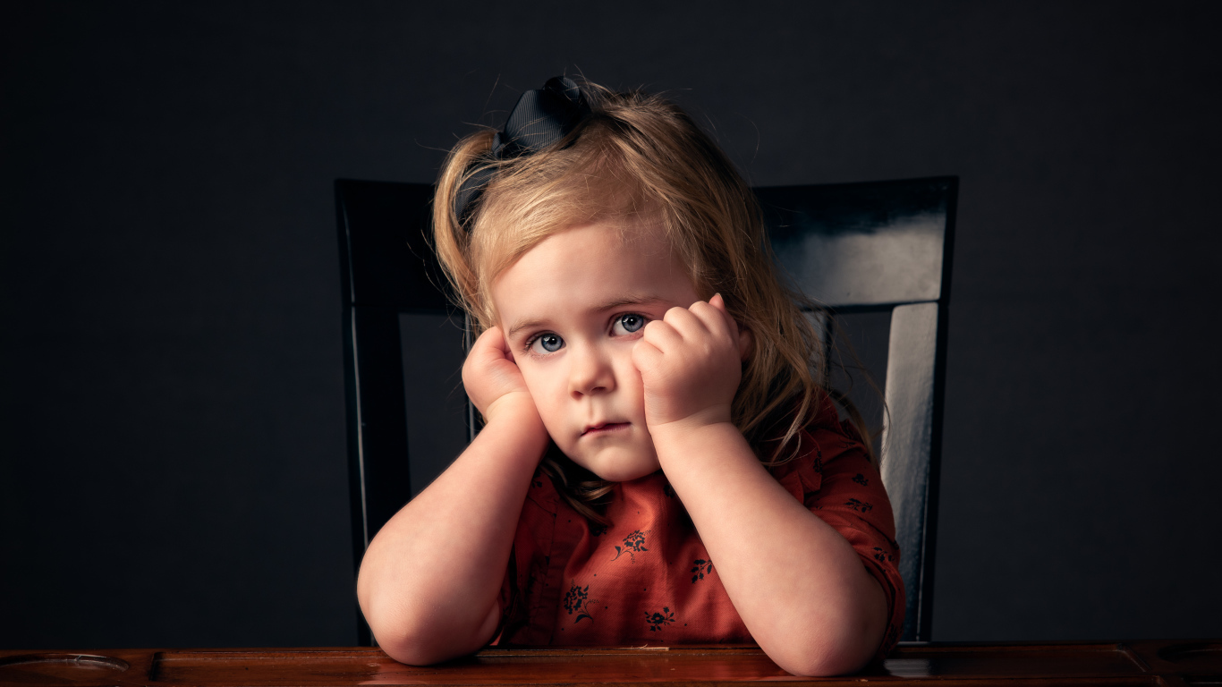 Грустная маленькая девочка сидит за столом