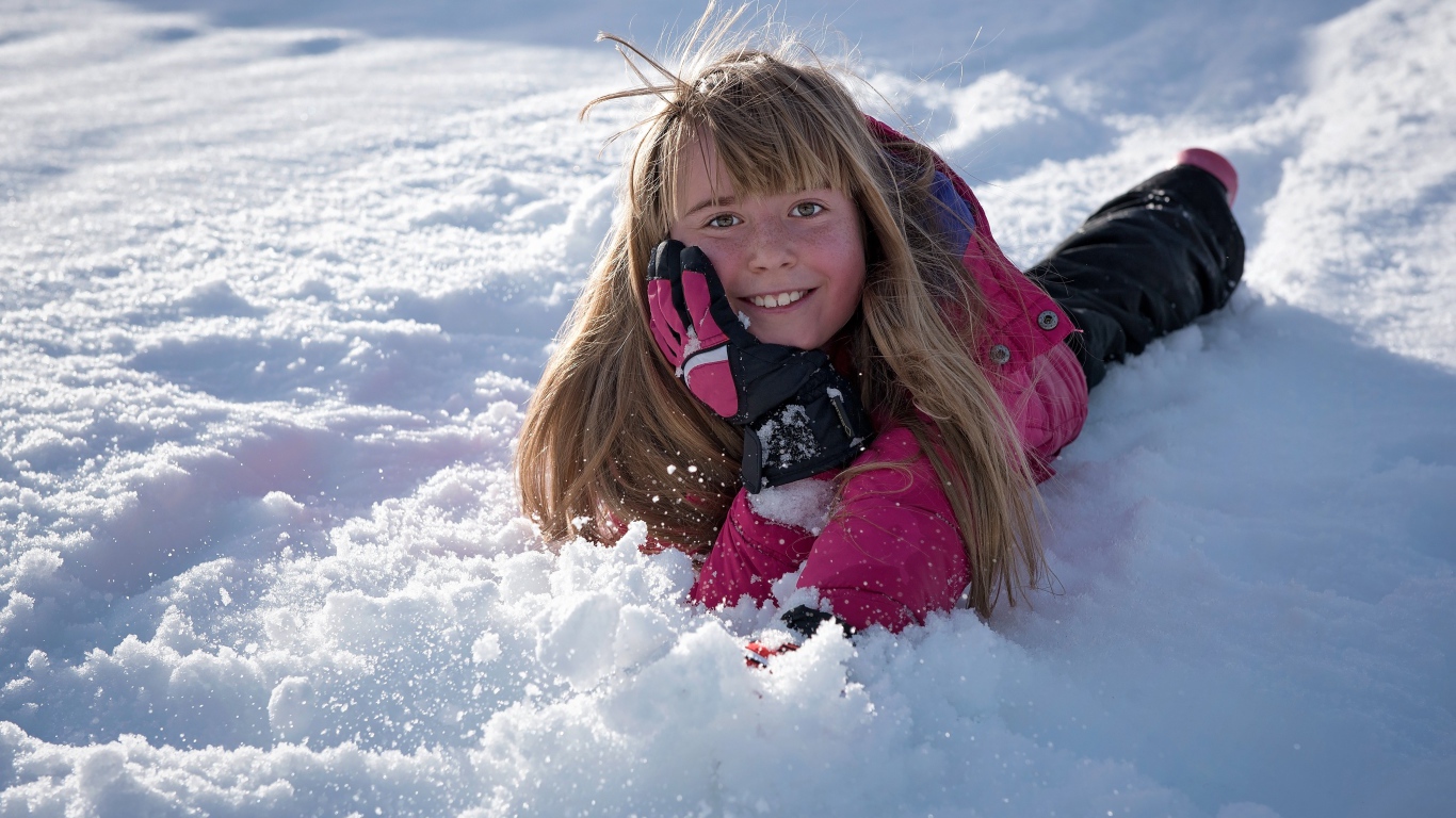 Улыбающаяся маленькая девочка лежит на снегу