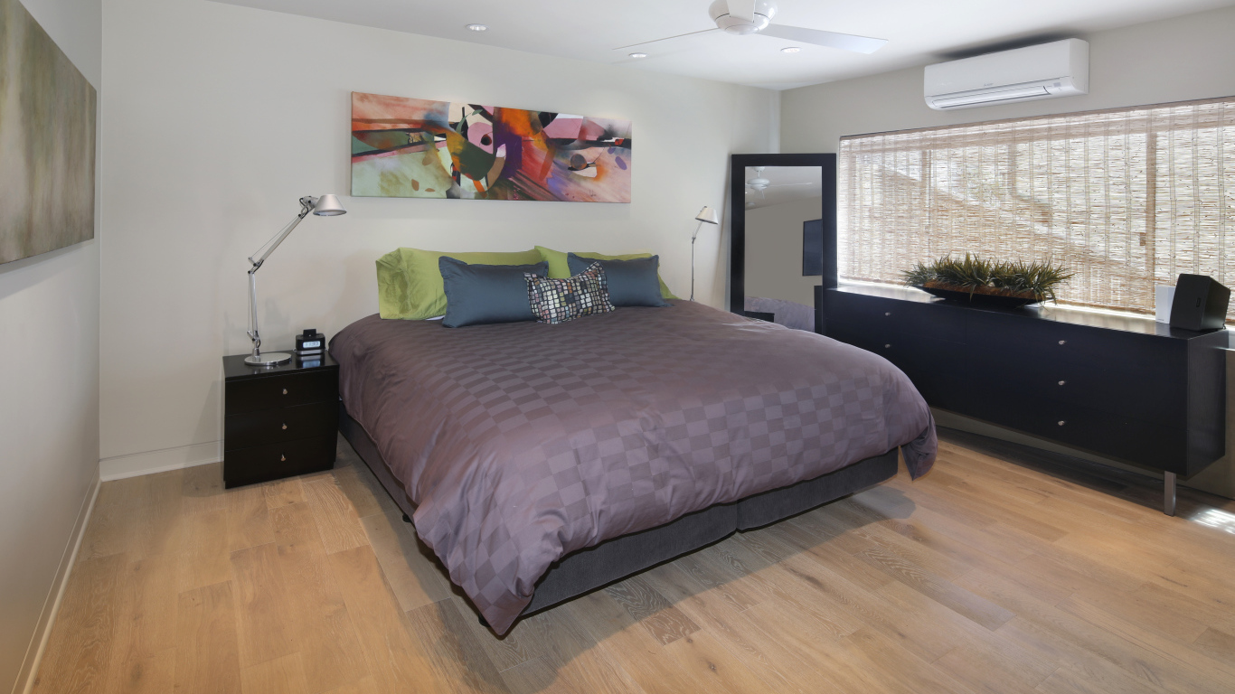 Большая серая кровать в спальне с белыми стенами