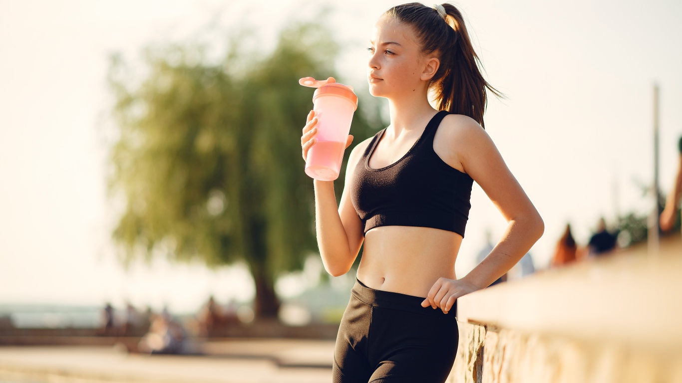 Спортивная девушка в черном пьет воду