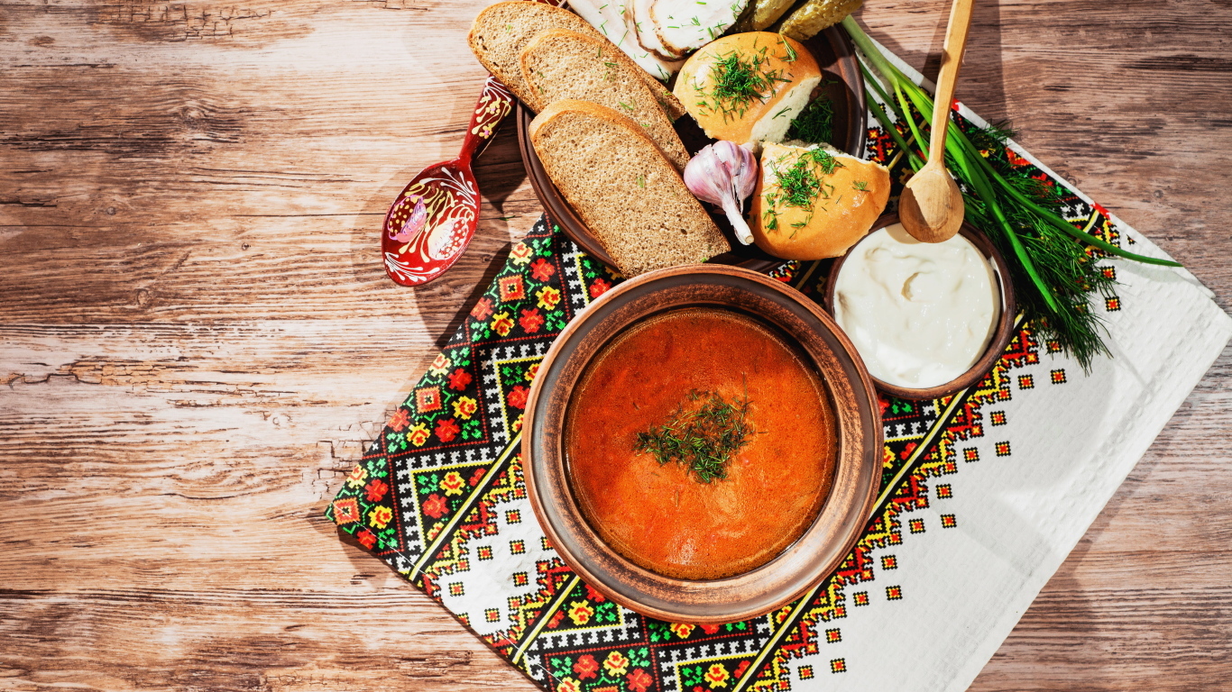 Тарелка борща на столе с салом, хлебом и зеленью