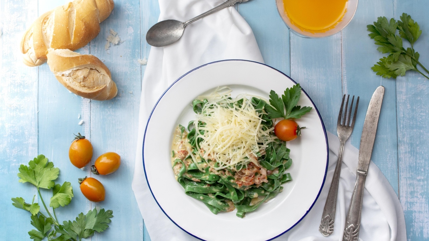 Зеленая лапша с сыром на столе с хлебом и зеленью