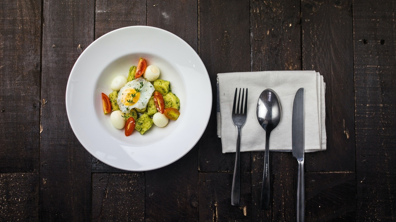 Яичница с овощами в белой тарелке на столе со столовыми приборами