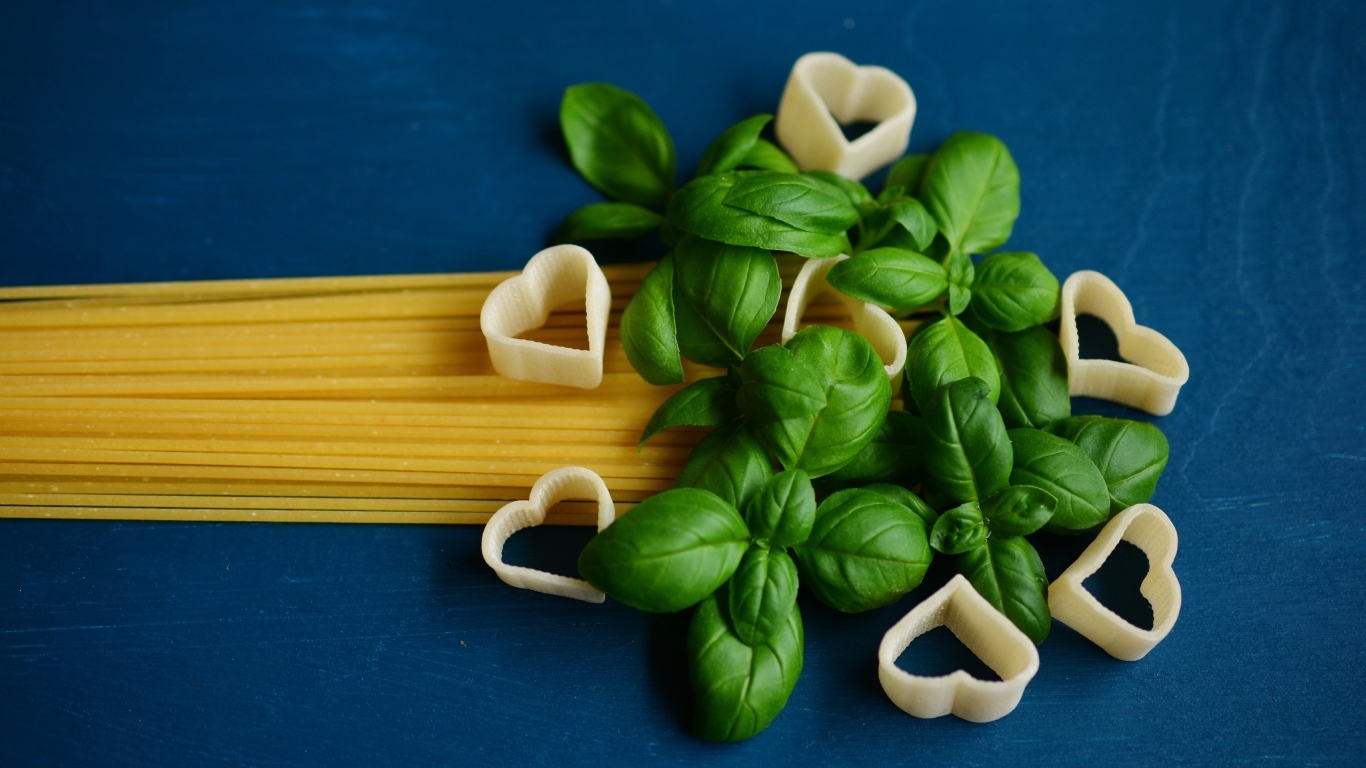 Спагетти на синем фоне с листьями базилика