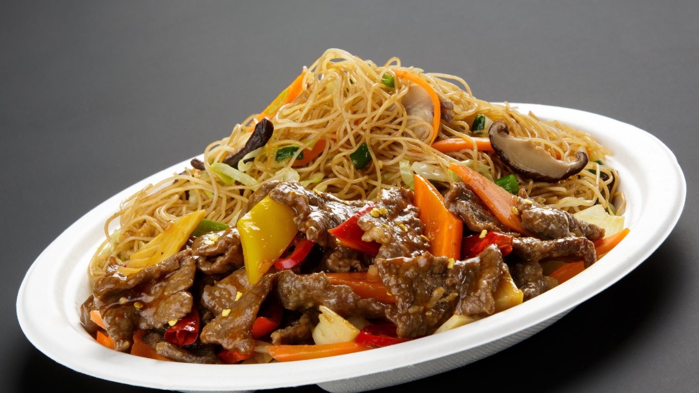 Острая лапша с грибами на белой тарелке на сером фоне