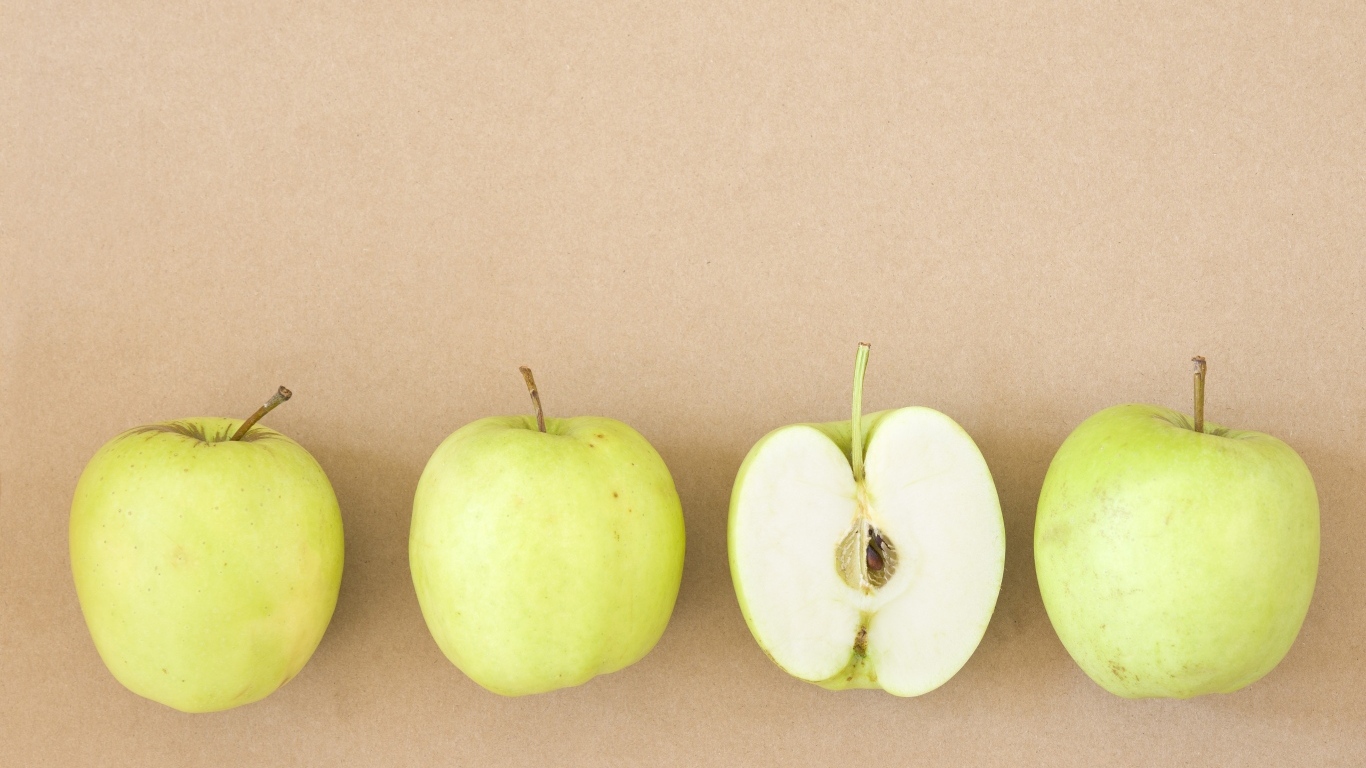 Четыре зеленых яблока на бежевом фоне 