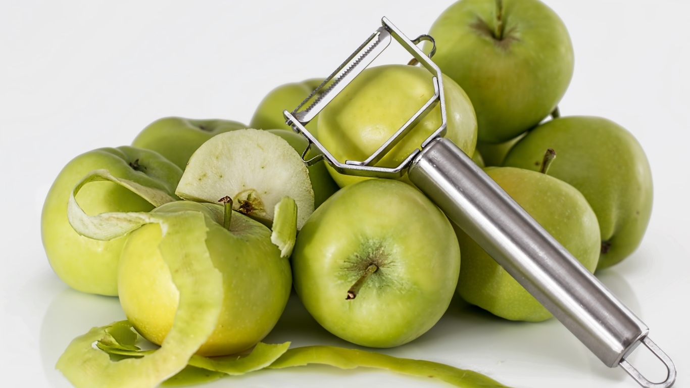 Зеленые яблоки с овощечисткой на белом фоне