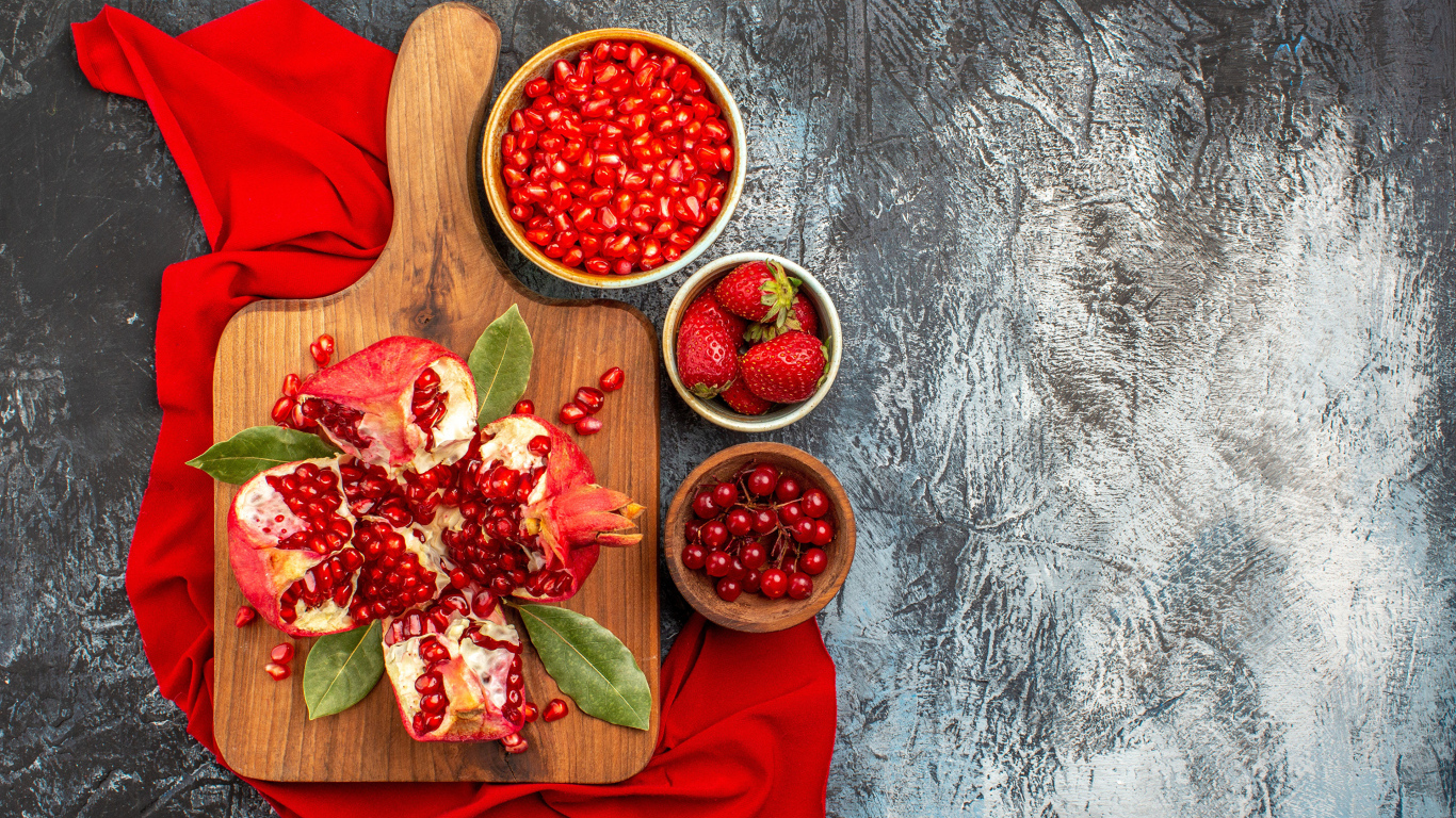 Очищенный гранат на столе с клубникой и ягодами смородины