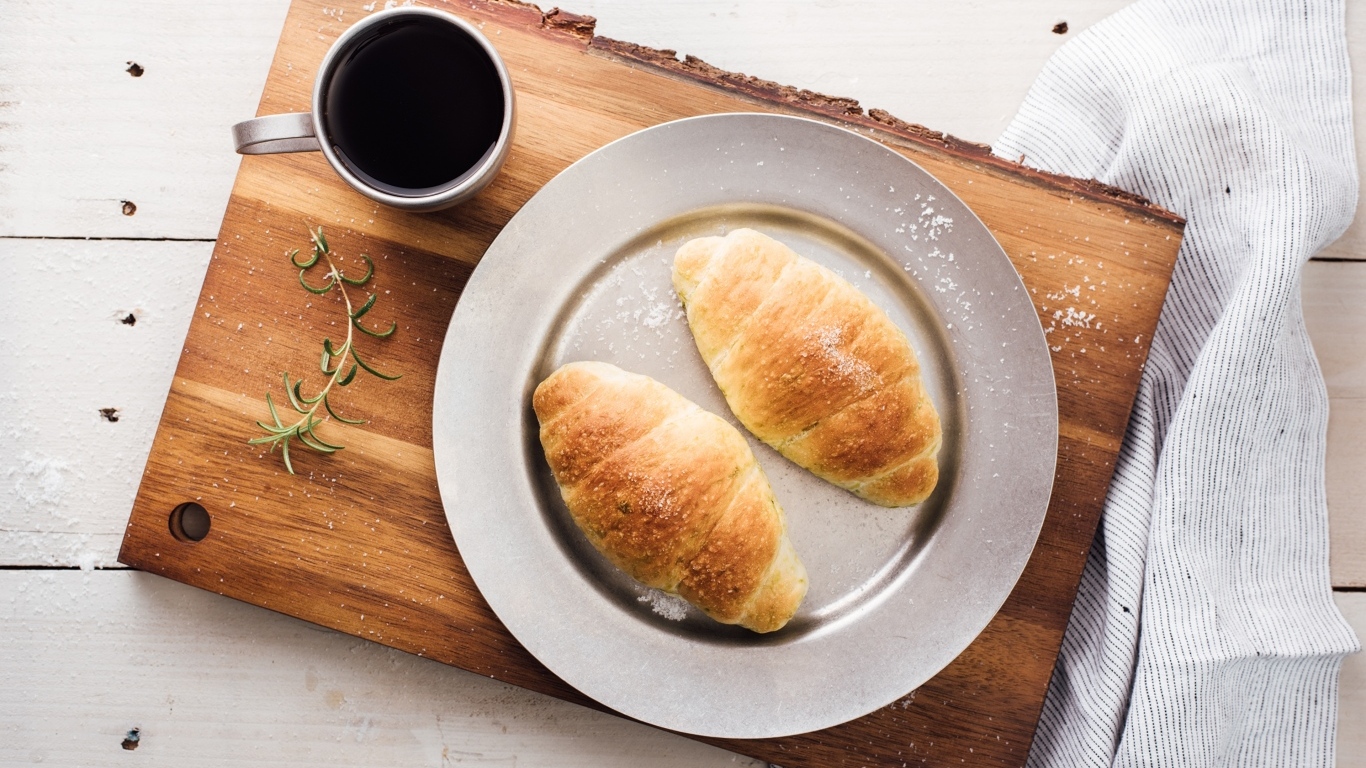 Два круассана на тарелке с чашкой кофе