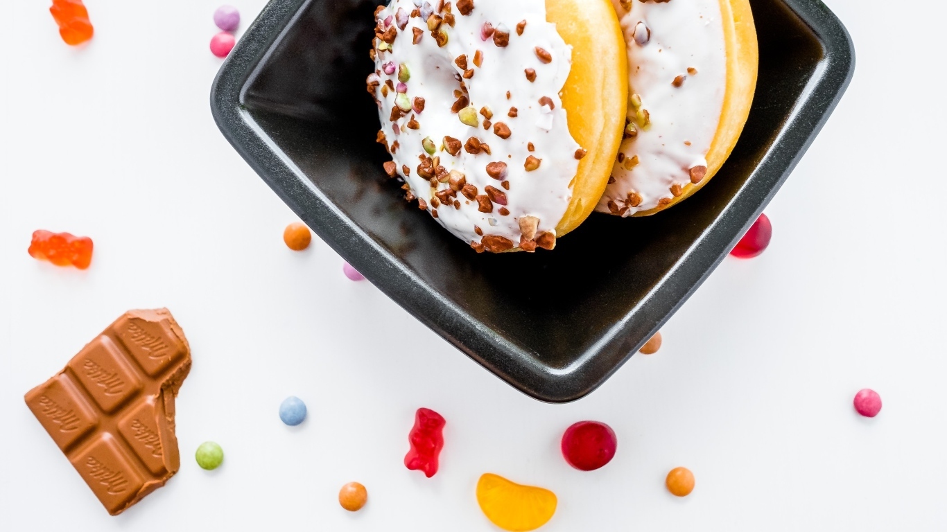 Два пончика в тарелке на белом фоне с конфетами